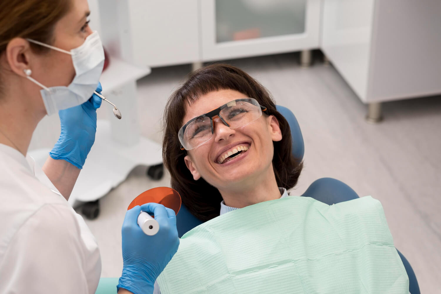 Paciente sorrindo e usando óculos de proteção durante consulta sobre indicação de cirurgia ortognática na Aliança Clínica Odontológica.