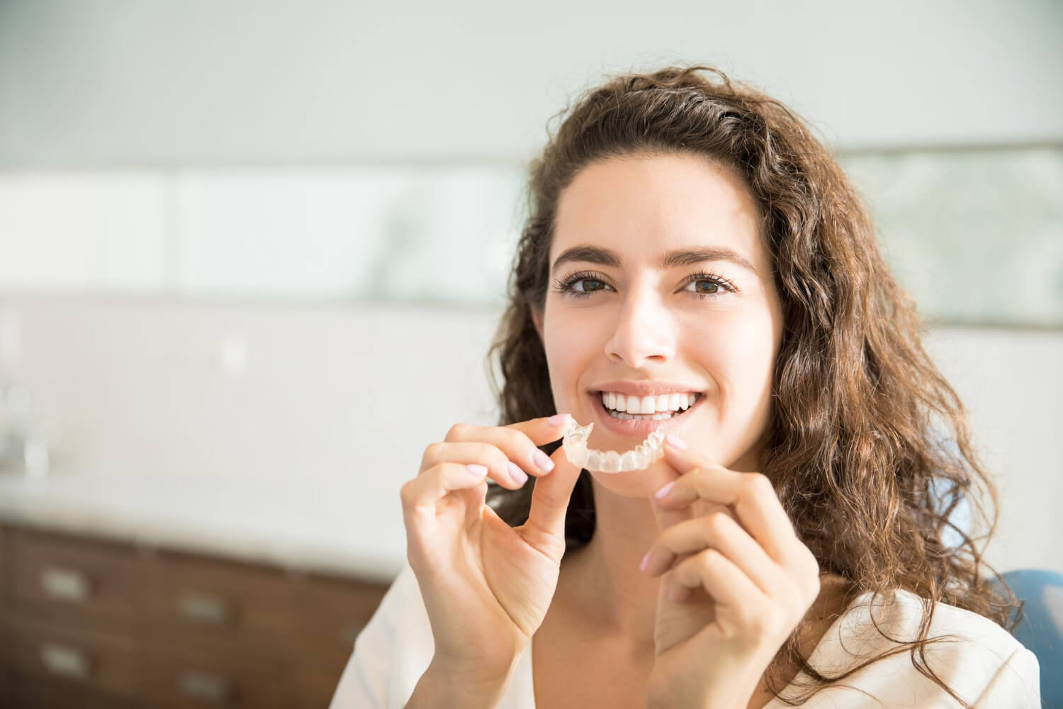 Mulher sorridente segurando um alinhador transparente ClearCorrect ou Invisalign na Aliança Clínica Odontológica em Nossa Sra da Glória.