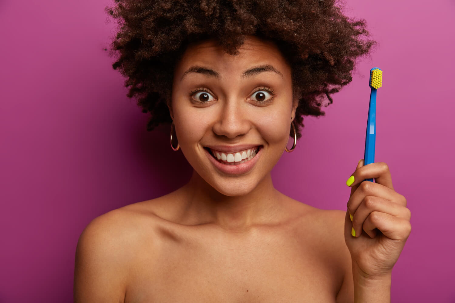 Mulher jovem sorridente segurando escova de dentes azul para higiene de aparelho e alinhadores na Aliança Odontologia em Nossa Sra da Glória.