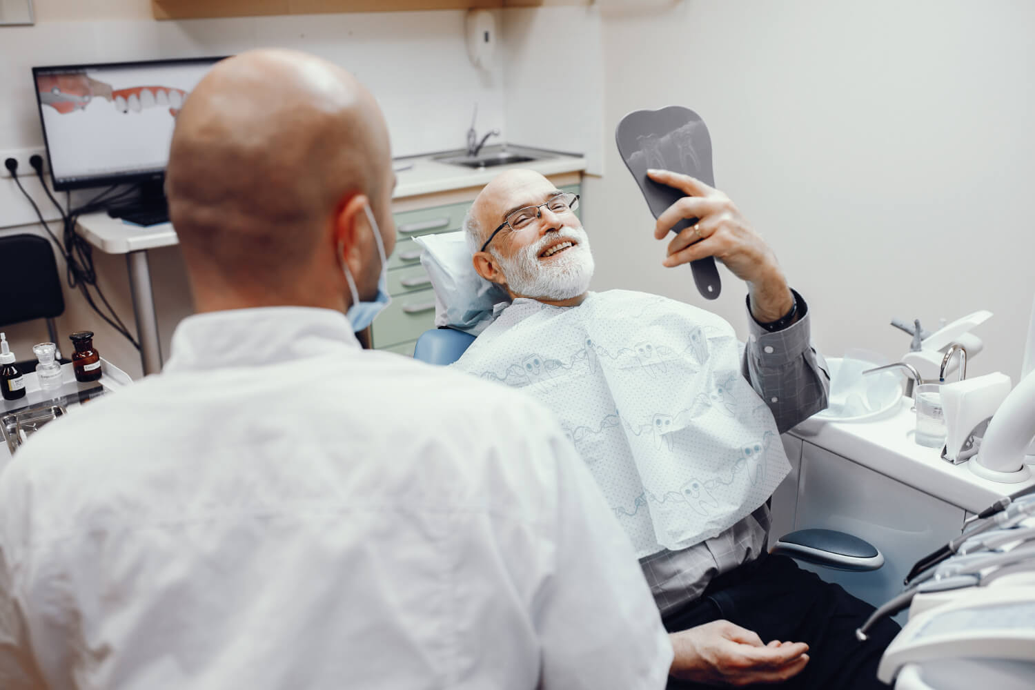 Paciente idoso sorridente observa implantes dentários no espelho após limpeza na Aliança Odontologia em Nossa Sra da Glória.